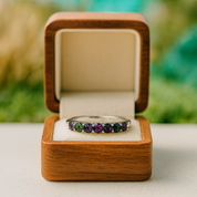 Ring with multicolored gemstones in a wooden box against a blurred natural background