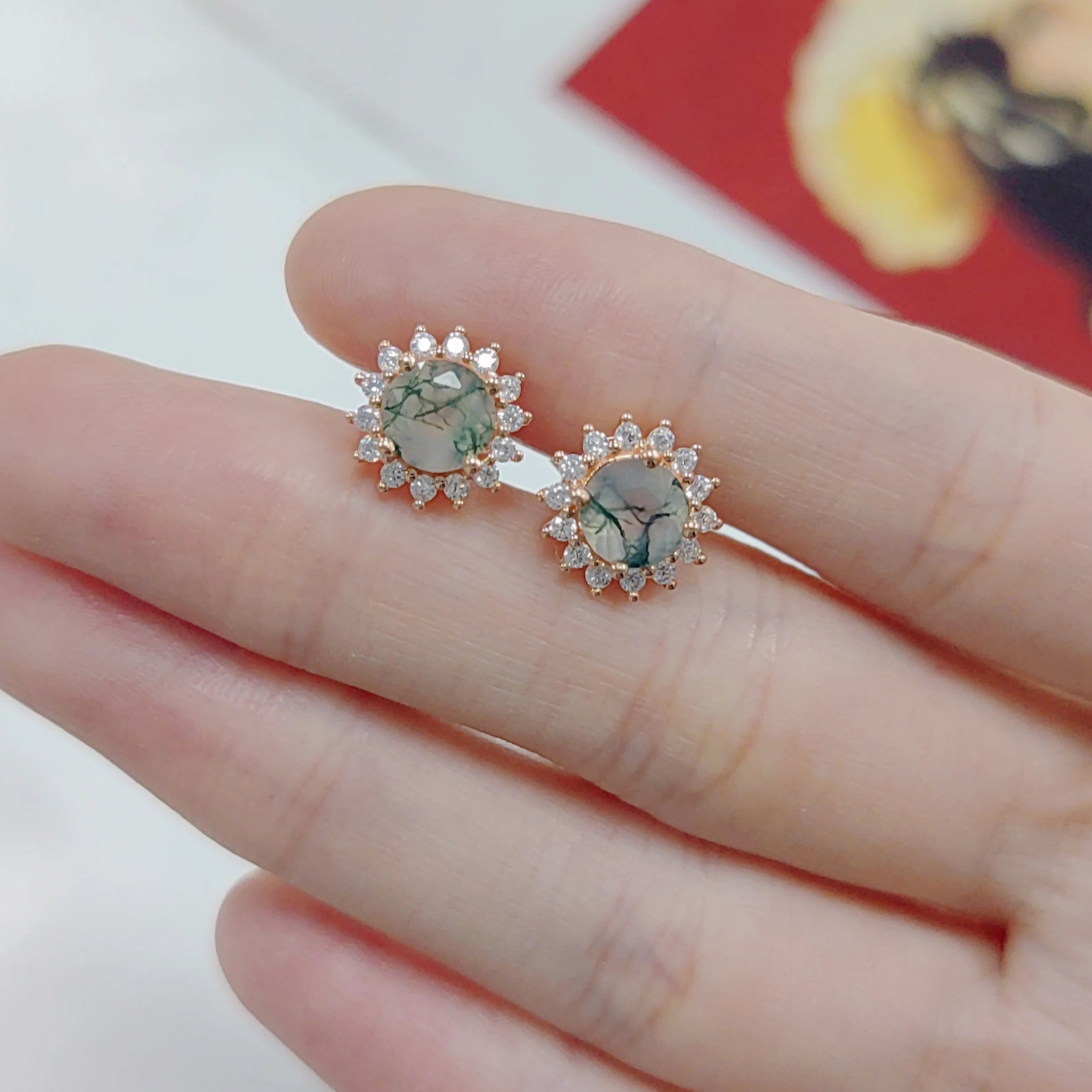 Rose gold earrings with gemstones held between fingers against a blurred background