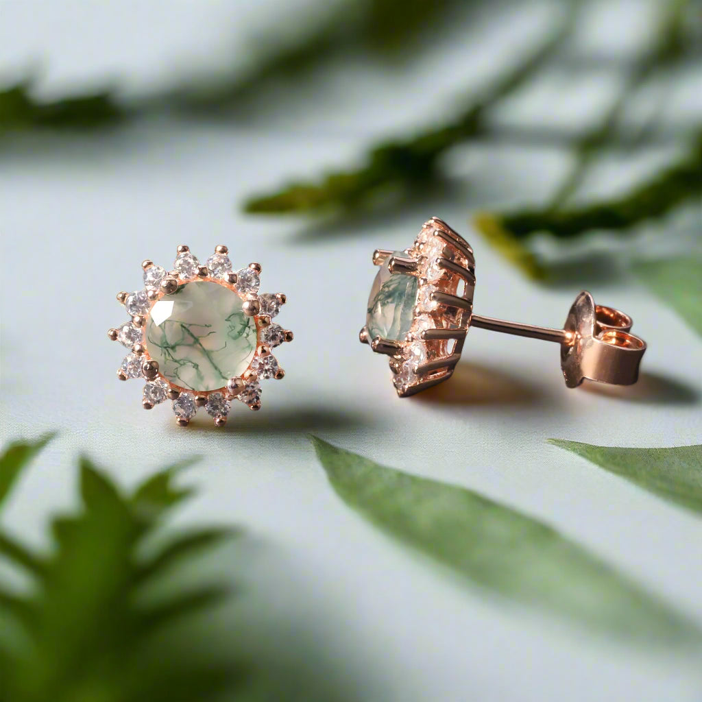 Rose gold earrings with green gemstones on a dark surface