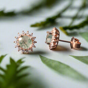 Rose gold earrings with green gemstones on a dark surface