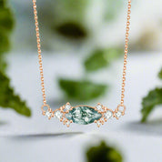 Rose gold necklace with a green gemstone and diamonds on a white background