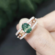 Rose gold ring with a green gemstone held in a hand against a blurred green background