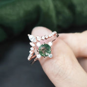 Rose gold ring with a green gemstone held in a hand against a blurred green background