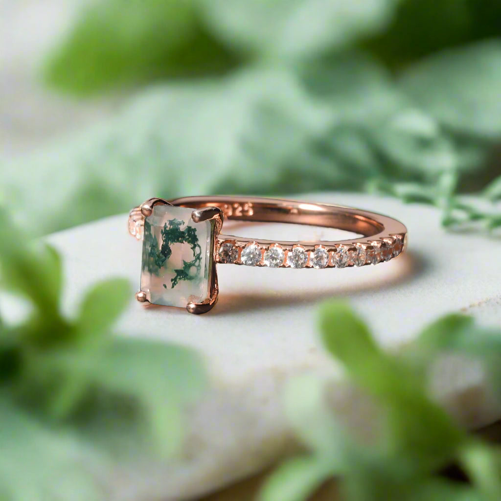 Rose gold ring with a green gemstone on a dark surface