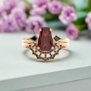 Rose gold ring with a red gemstone and black gemstones on a white background