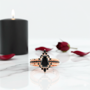 Rose gold ring with black gemstone on a marble surface with a black candle and red roses in the background.