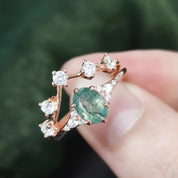 Rose gold ring with emerald and diamonds held on a blurred green background