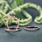 Rose gold ring with green gemstone and diamond-studded band on a dark background