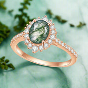Rose gold ring with green gemstone and diamond accents on a white background