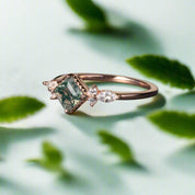 Rose gold ring with green gemstone and diamonds on a dark surface