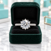 A radiant-cut diamond engagement ring with a pavé band, displayed in an open dark green velvet ring box on a white marble surface.