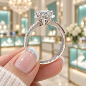 A close-up of a silver-toned diamond engagement ring held between fingers in a bright jewelry store with turquoise display cases in the blurred background.