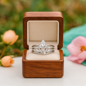 Set of silver rings with a diamond in a wooden box, surrounded by flowers.