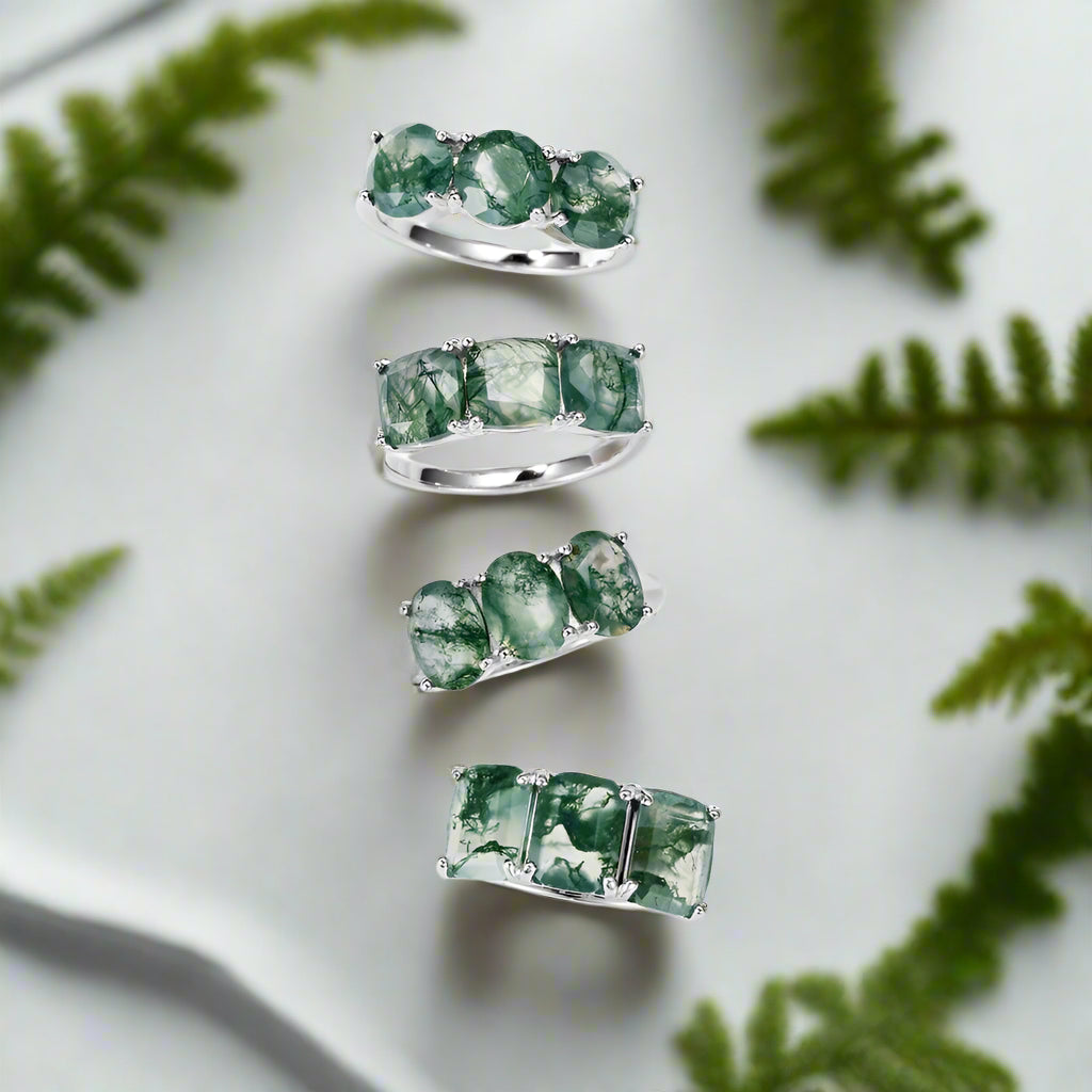 Set of silver rings with green gemstones on a light background with greenery.