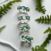 Set of silver rings with green gemstones on a light background with greenery.