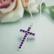 Silver cross necklace with purple stones on a light green background with a blurred rose.