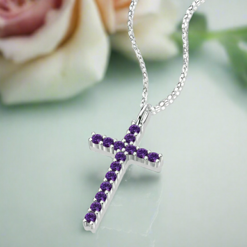Silver cross necklace with purple stones on a light green background with a blurred rose.