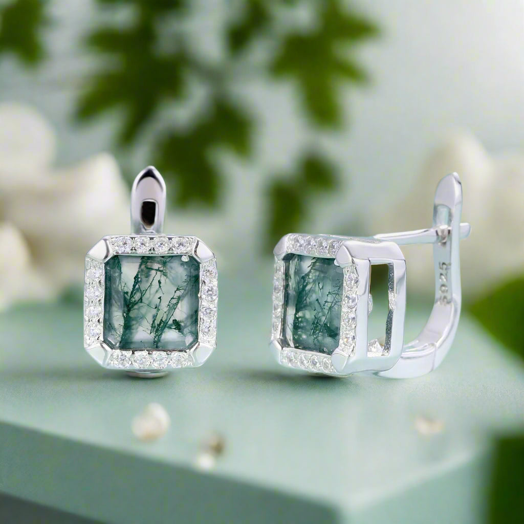 Silver earrings with green gemstones on a light blue background