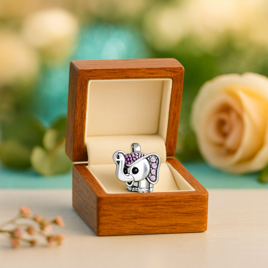 Silver elephant charm with pink stones in a wooden box against a blurred natural background