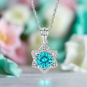 Silver necklace with a blue heart-shaped pendant against a blurred floral background