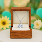 Silver necklace with a diamond pendant in an open wooden box against a blurred floral background