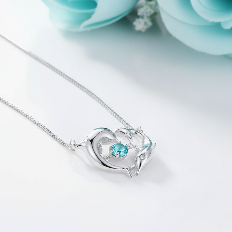 Silver necklace with a dolphin-shaped pendant featuring a blue gemstone on a light blue background.