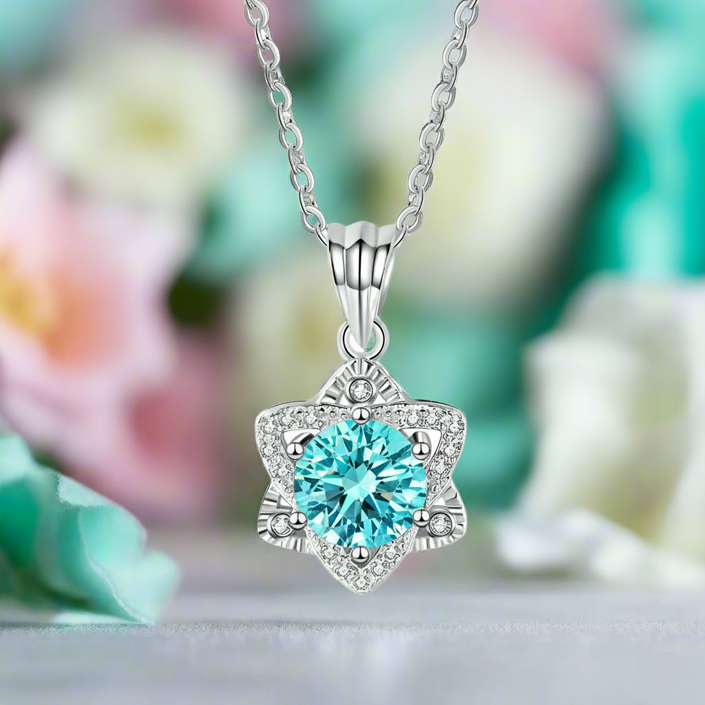 Silver necklace with a heart-shaped blue gemstone pendant against a blurred floral background