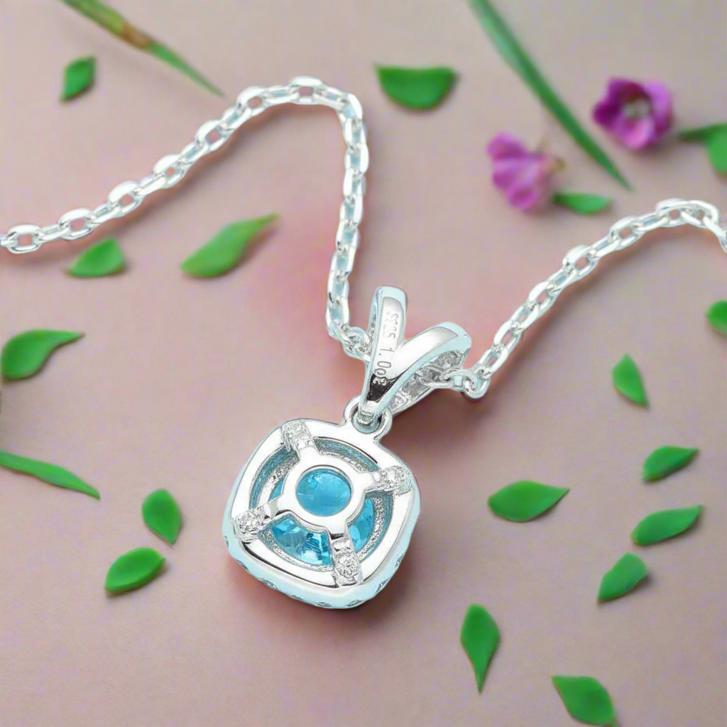 Silver necklace with a heart-shaped pendant featuring a blue gem on a light blue background