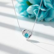 Silver necklace with a heart-shaped pendant featuring a blue gemstone on a white background
