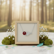 Silver necklace with a red gemstone on a display box in a forest setting