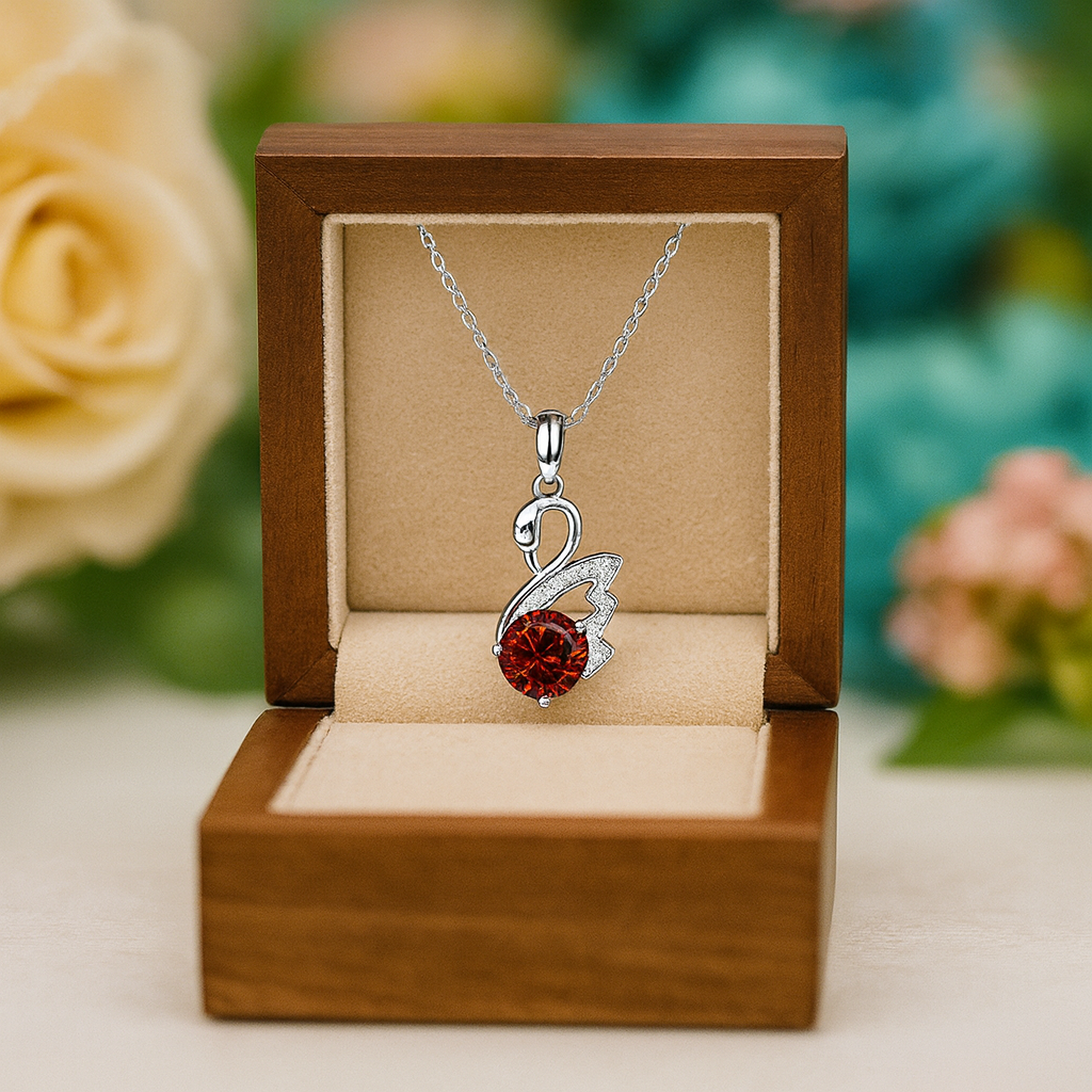 Silver necklace with a red gemstone pendant in a wooden box with flowers in the background