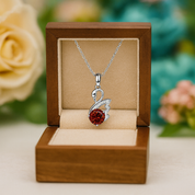 Silver necklace with a red gemstone pendant in a wooden box with flowers in the background