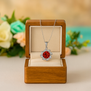Silver necklace with a red pendant in a wooden box with flowers in the background