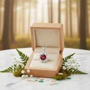 Silver necklace with a red pendant in an open wooden box on a white surface with greenery.