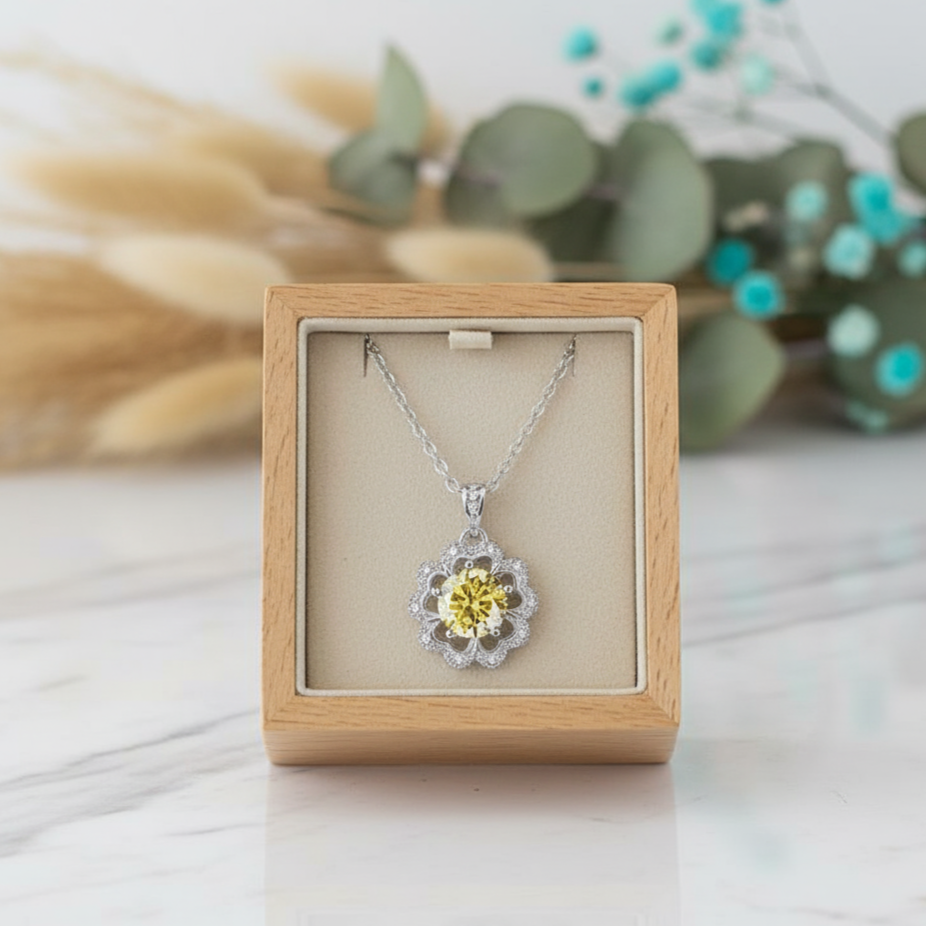 Silver necklace with a yellow center pendant in a wooden box on a light surface with greenery in the background