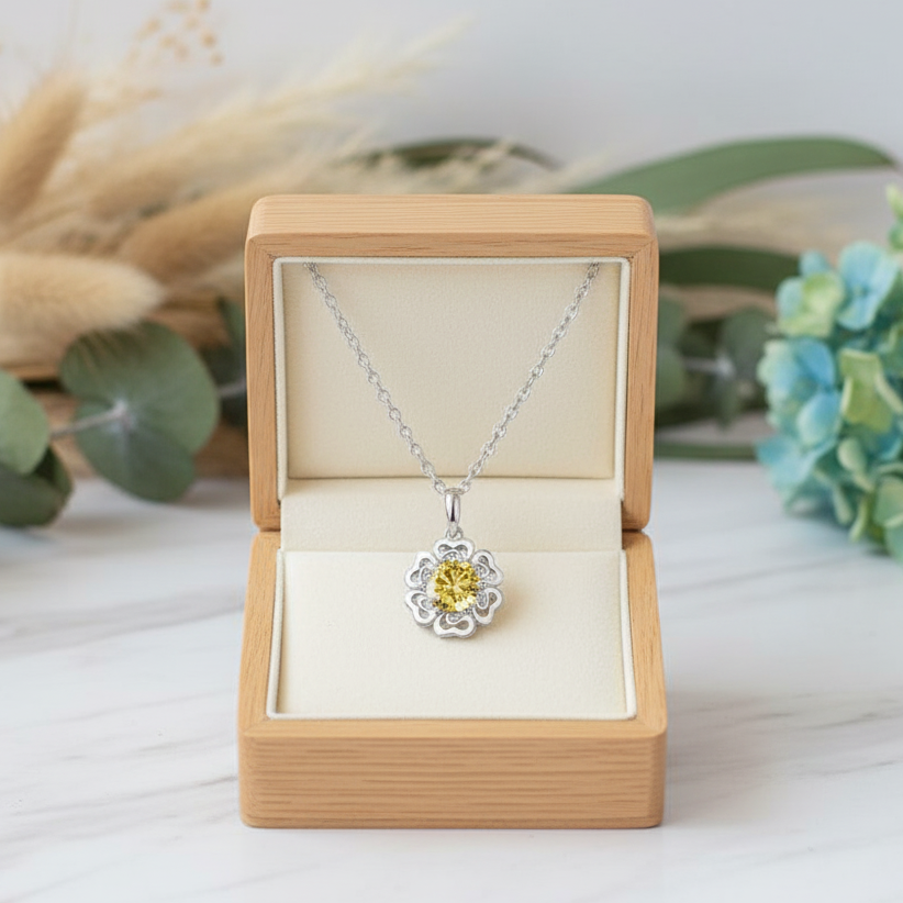 Silver necklace with a yellow pendant in an open wooden box on a light surface with decorative elements.