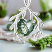 Silver pendant with a green heart-shaped gem on a white background