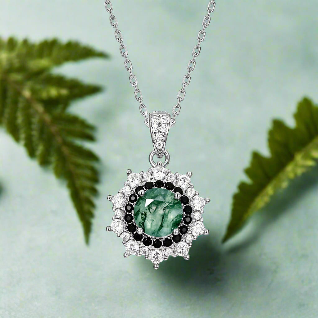 Silver pendant with green gemstone and black stones on a white background