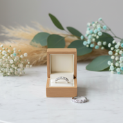 Silver ring in a wooden box on a marble surface with decorative plants.