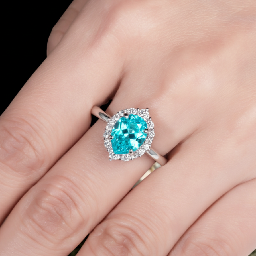 Silver ring with a blue gemstone on a hand against a black background