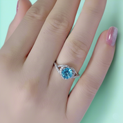 Silver ring with a blue gemstone on a hand against a light green background