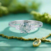 Silver ring with a central gemstone and two smaller stones on a light blue background