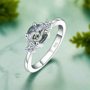 Silver ring with a green gemstone and diamonds on a white background