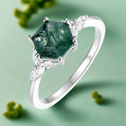 Silver ring with a green gemstone and diamonds on a white background