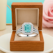 Silver ring with a green gemstone in a wooden box on a light surface with a blurred pink rose in the background.