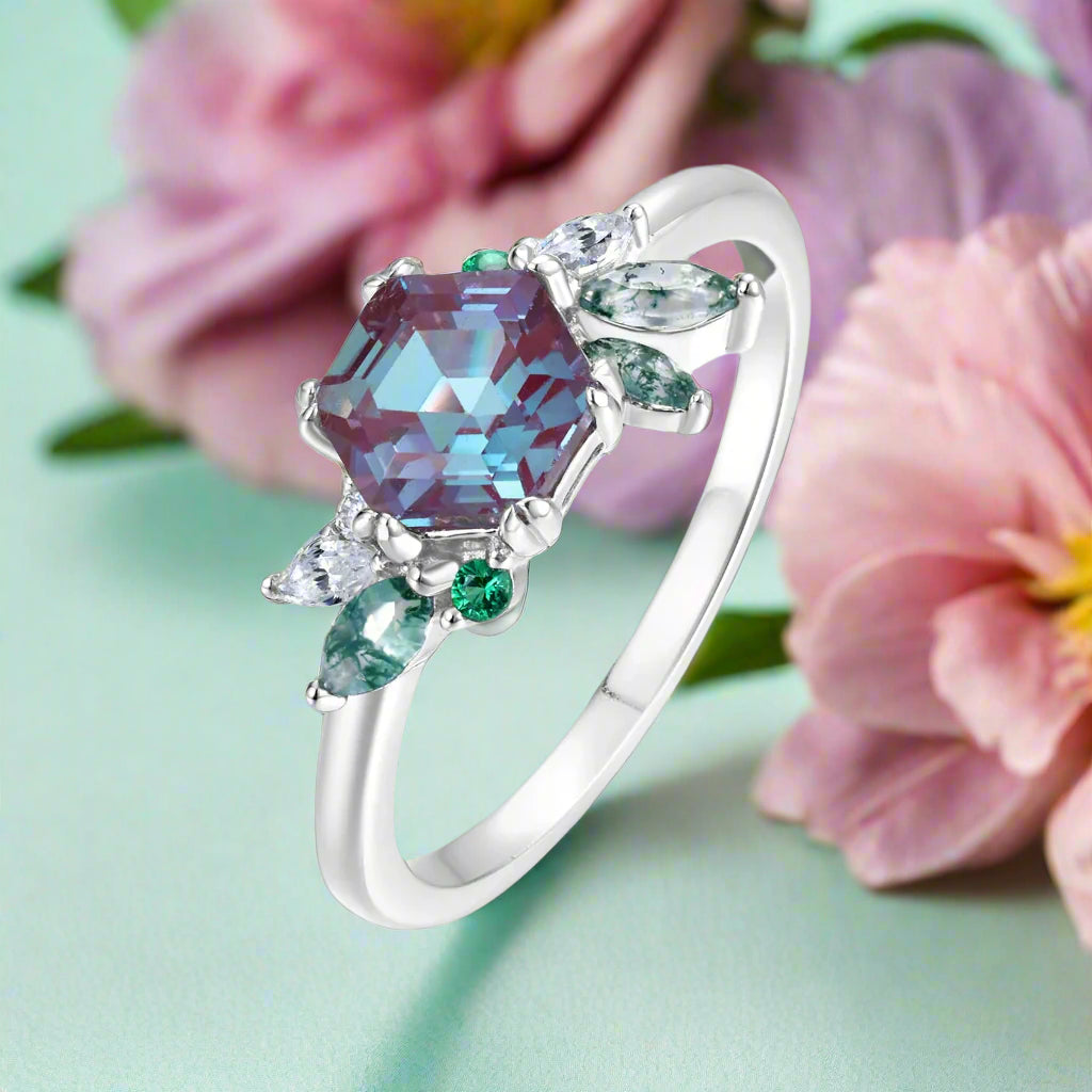 Silver ring with a large purple gemstone and smaller green and clear stones on a white background