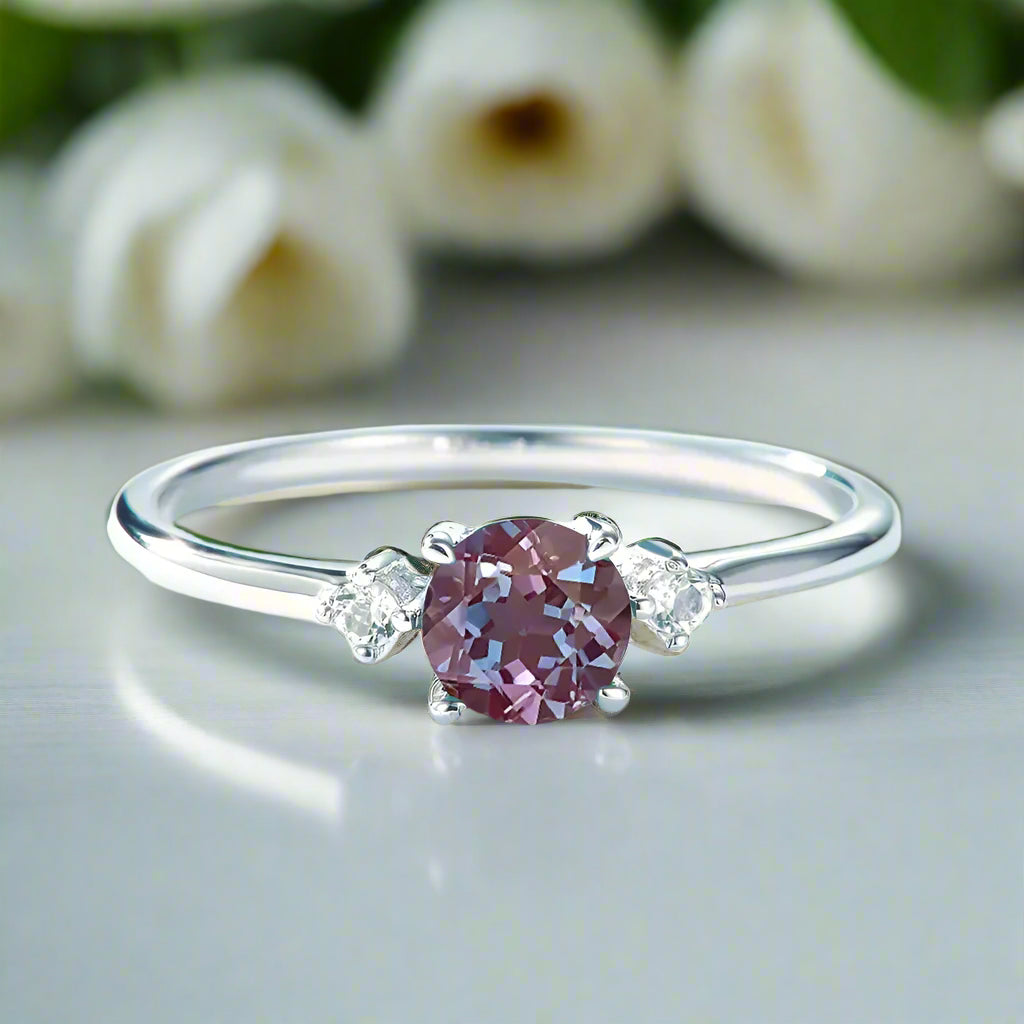 Silver ring with a pink gemstone and two smaller diamonds on a light blue background