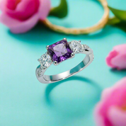 Silver ring with a purple gemstone and smaller clear stones on a light blue background