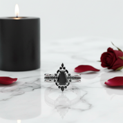 Silver ring with black gemstone on a marble surface with a black candle and red rose petals.