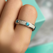 Silver ring with blue gemstones on a finger against a teal background